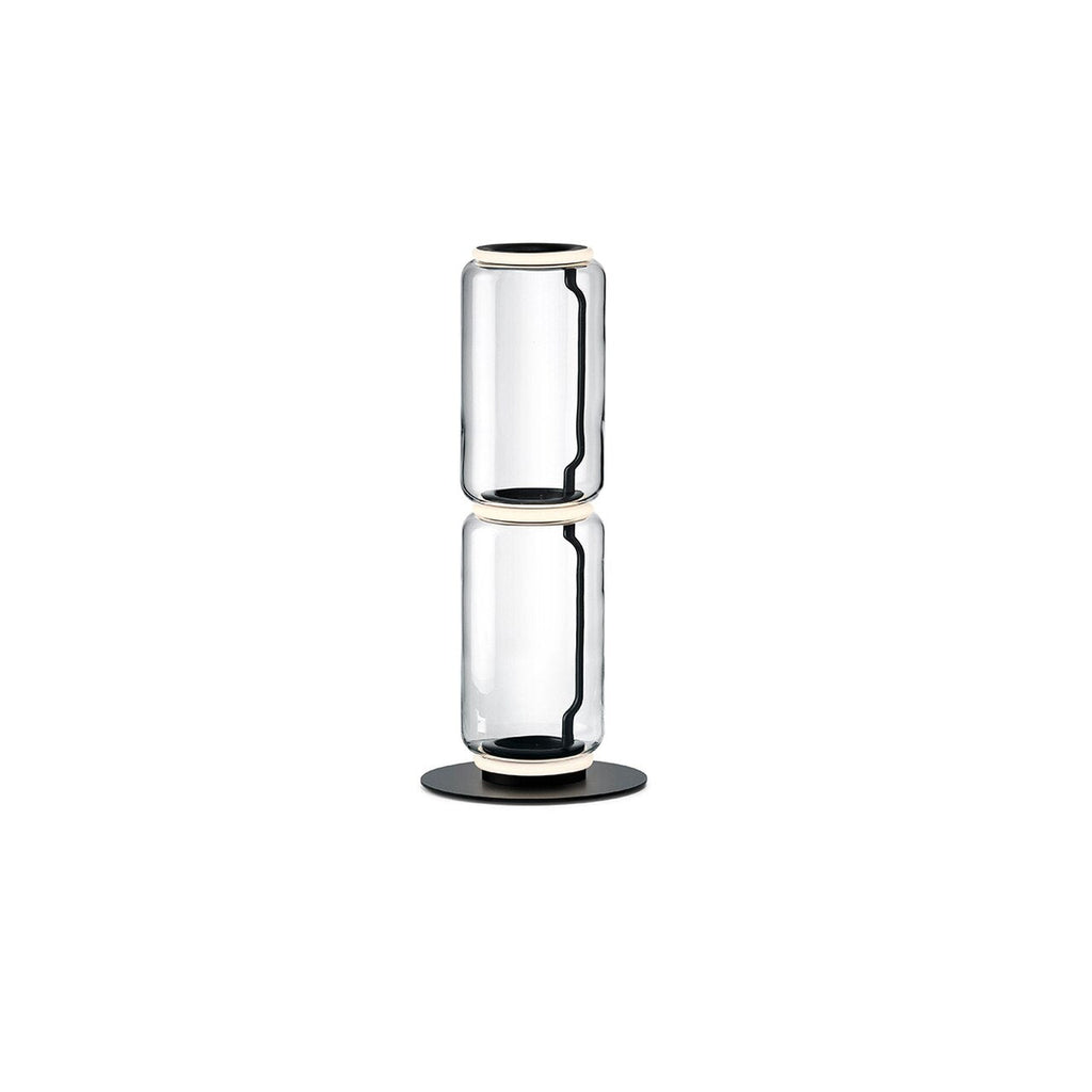 Two-cylinder Clérachic floor lamp on a white backdrop, clear glass drums joined by a glowing ring on a round black base.