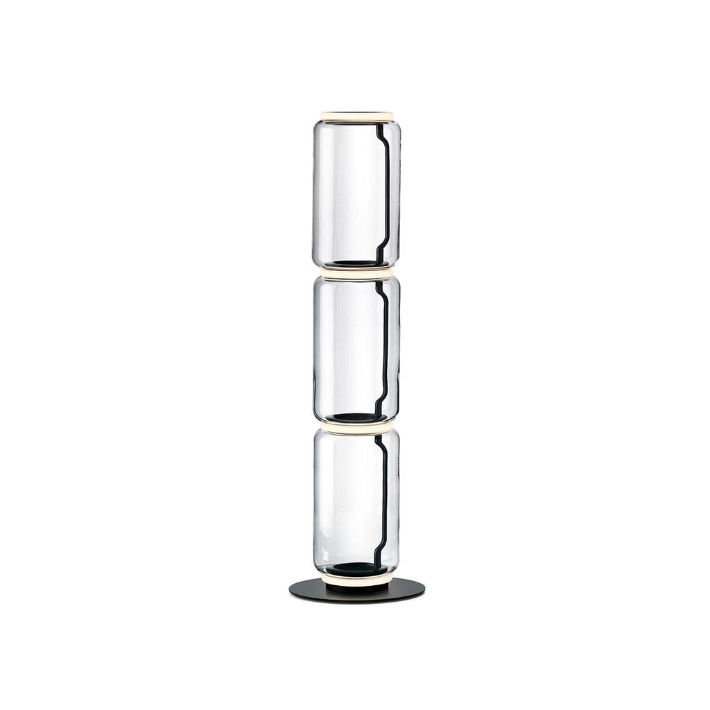 Clérachic floor lamp on white, three stacked clear glass cylinders with glowing rings at each join and a round black base.