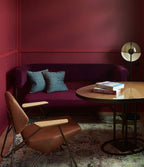 Floor lamp with a half-open dome in the corner of a burgundy room with a plum sofa, a brown armchair and a round table; from Clérachic.
