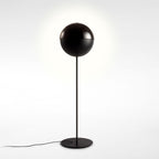 Black floor lamp with its dome closed into a full sphere on a thin stem, on a soft white backdrop; this Clérachic design.
