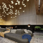 Floor lamp glowing in front of a low grey sofa, with clustered ceiling lights and timber walls above; a Clérachic piece.