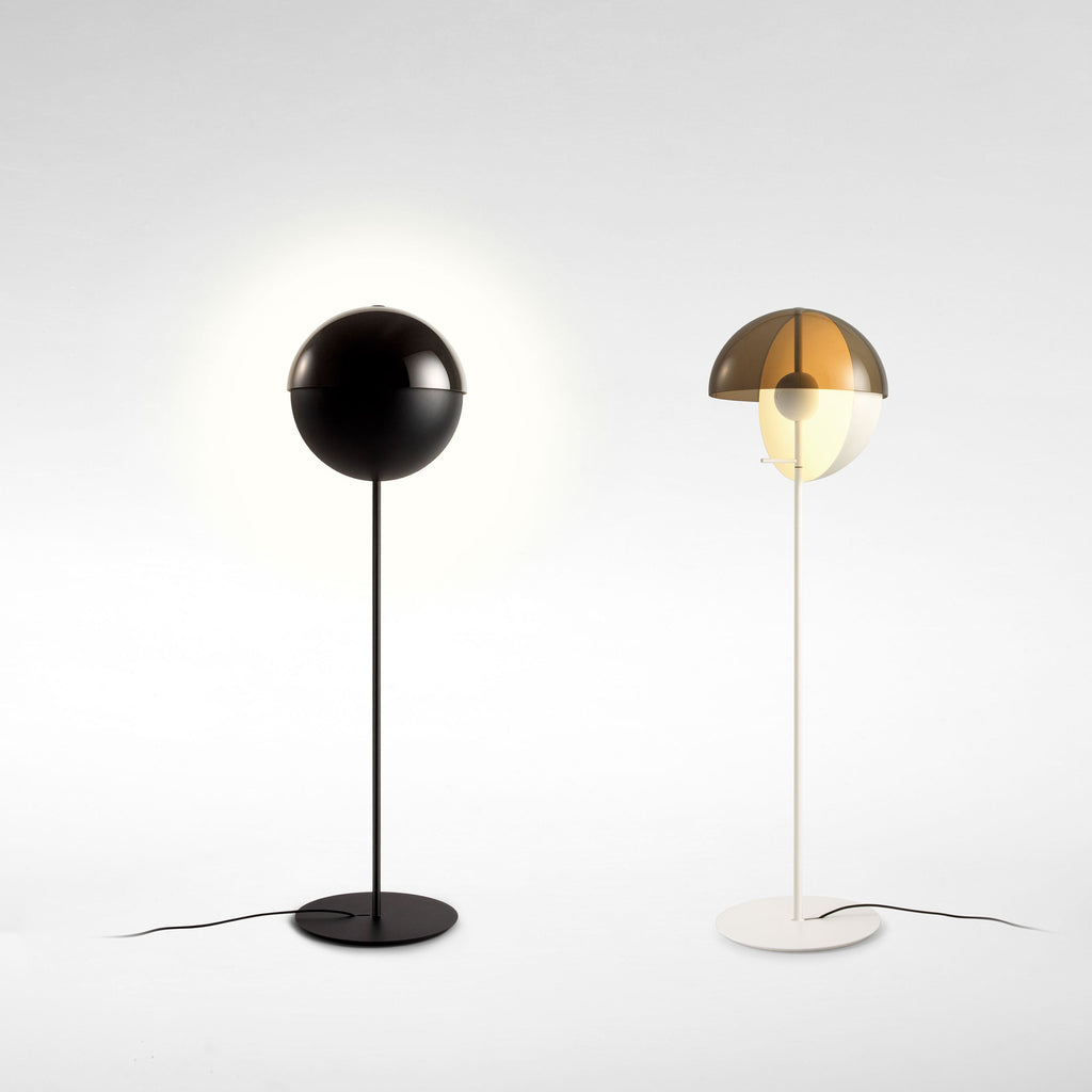Two Clérachic floor lamps side by side, a black one with its dome closed and glowing, and a white one with its dome open.