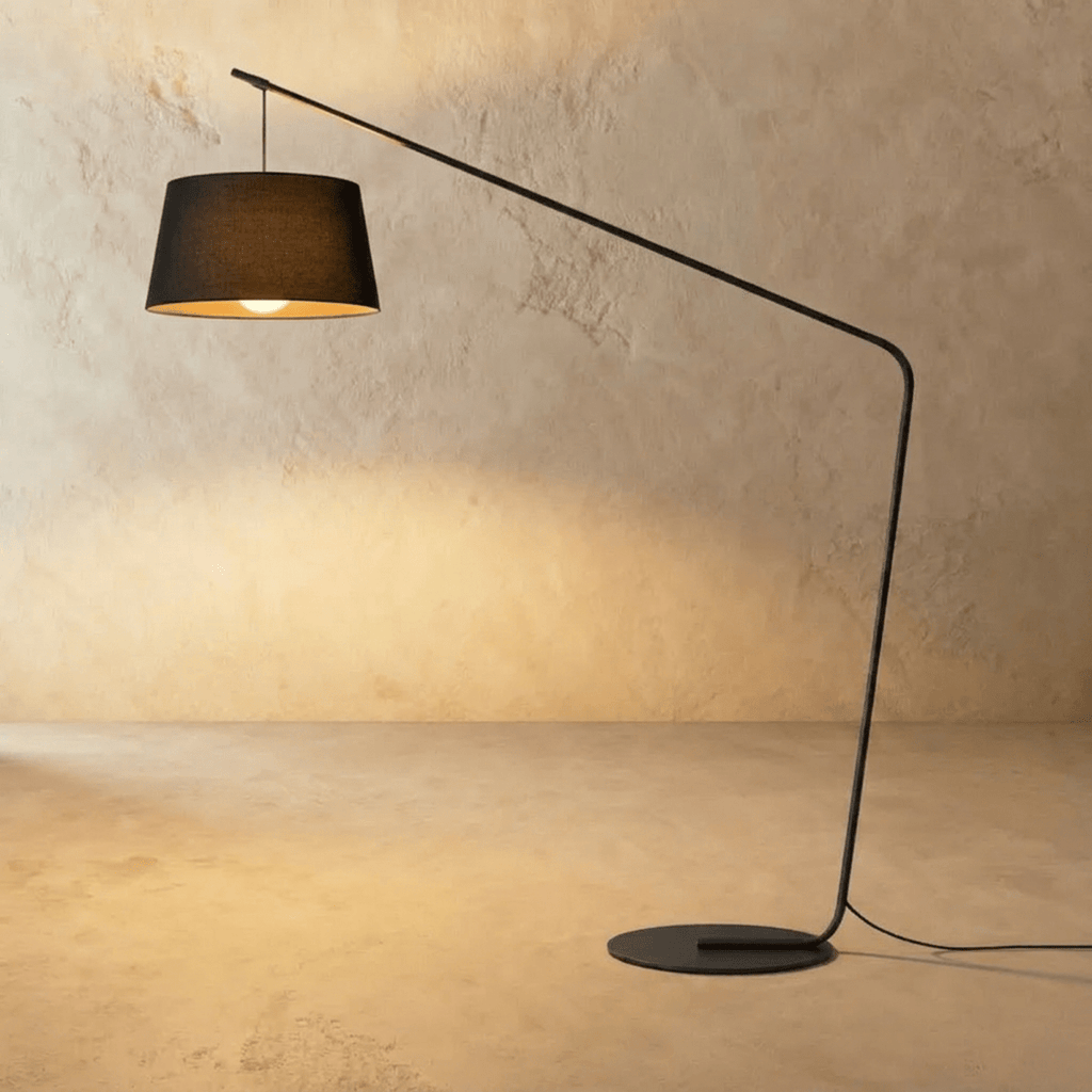 Clérachic arc floor lamp with a black tapered fabric shade, a long slim black arm and a round flat base on limewash.