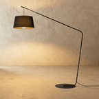 Clérachic arc floor lamp with a black tapered fabric shade, a long slim black arm and a round flat base on limewash.
