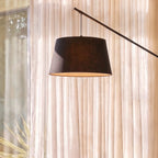 Close view of the Clérachic black tapered fabric shade hanging from a slim black arm against pleated sheer curtains.