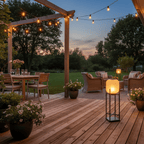 Lit Clérachic floor lantern on a wooden deck under a pergola at dusk, with string lights and a laid dining table behind.