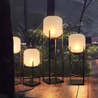 Close view of three lit Clérachic lanterns of different heights on a wooden deck among palm leaves at night.