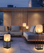 Clérachic lanterns glowing on a paved terrace by a grey outdoor sofa, with a slatted screen and city towers behind.