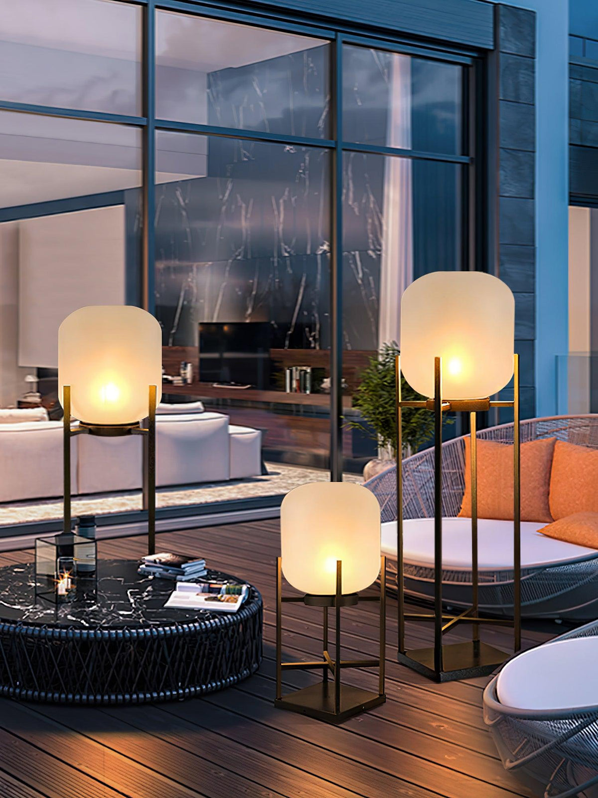 Lit Clérachic lanterns beside a round rattan chair and a dark coffee table in front of tall glazed doors at dusk.