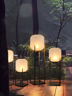 Group of three lit Clérachic lanterns on a deck among ferns and trees, with a fourth edging into the frame at left.