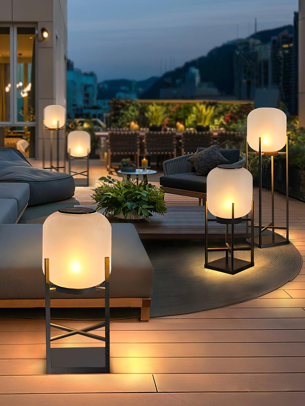 Clérachic lantern in the foreground on a deck, with more lit lanterns around a low sofa and a plant beyond it.