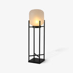 Angled view of this Clérachic lantern lit on a pale grey background, with its frosted shade and black cross-braced frame.