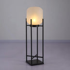 This Clérachic lantern lit on a grey studio floor against a lilac-grey wall, with a frosted shade on a black frame.