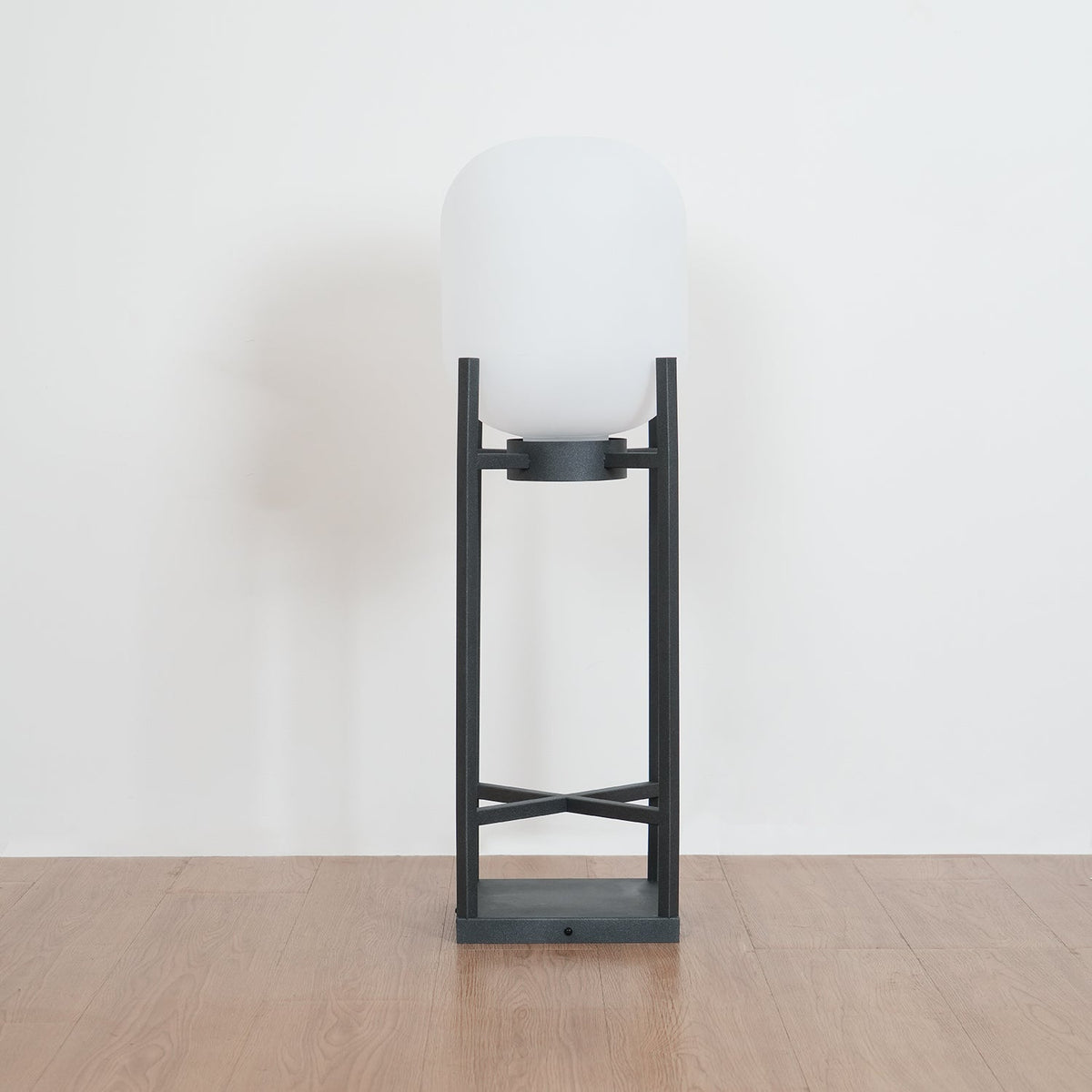 Unlit Clérachic lantern with a white glass shade on a charcoal frame, standing on a wooden floor against a pale wall.