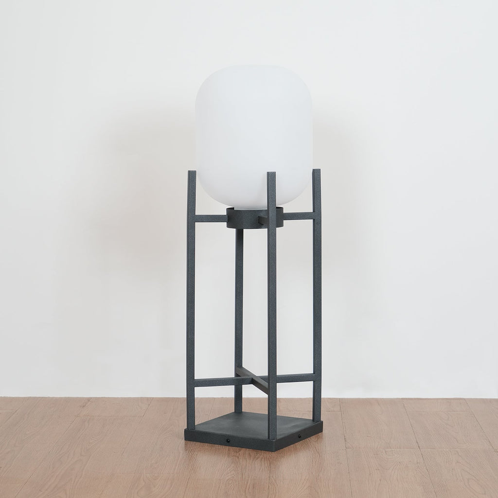 Slightly angled view of this Clérachic lantern unlit on a wooden floor, with its white shade and charcoal four-post frame.