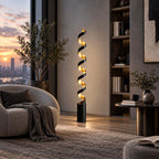 At dusk, this Clérachic spiral floor lamp glows beside a bookshelf and a round dark side table, with a city skyline in the window.