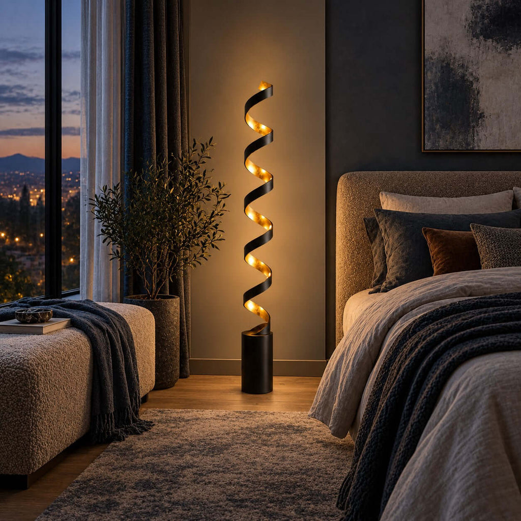 Close to a bed with a chunky grey knit throw, this Clérachic black and gold spiral floor lamp glows against a dark wall and a tall plant.