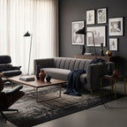 Clérachic floor lamp behind a grey channel-tufted sofa in a dark-walled living room hung with framed prints.