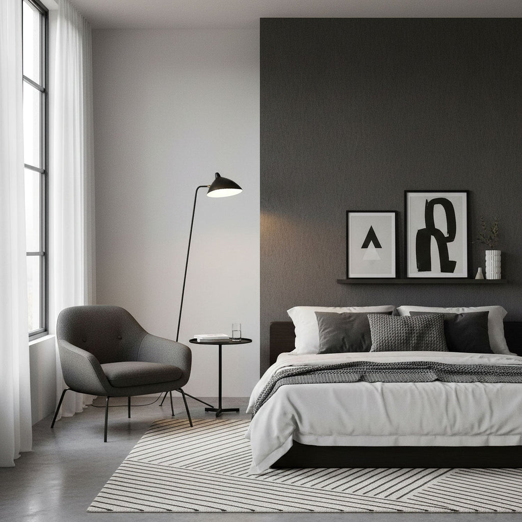 A Clérachic floor lamp leans over a small armchair beside a grey bed, against a dark charcoal feature wall.