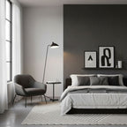 A Clérachic floor lamp leans over a small armchair beside a grey bed, against a dark charcoal feature wall.