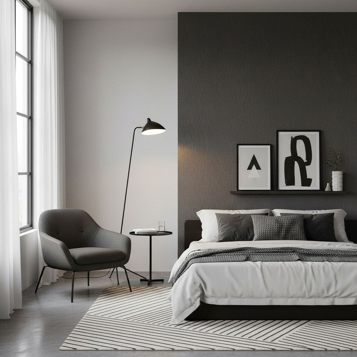 A Clérachic floor lamp leans over a small armchair beside a grey bed, against a dark charcoal feature wall.