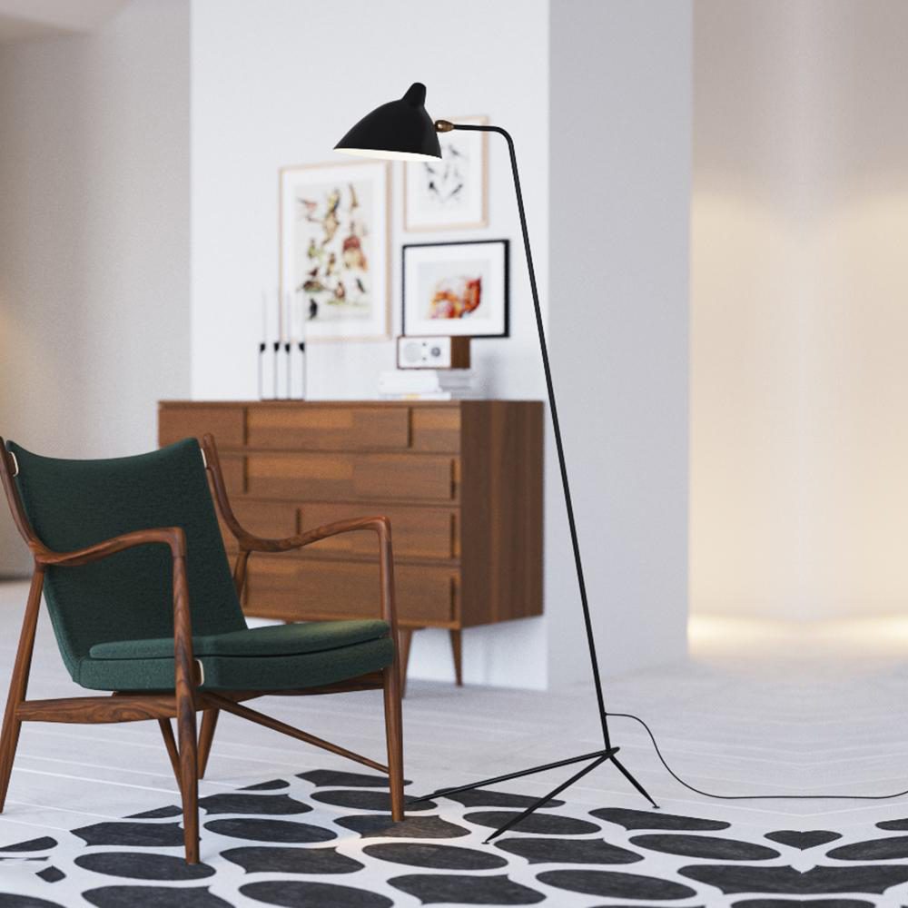 Black Clérachic floor lamp with a tripod base, standing beside a green chair and a walnut chest of drawers.