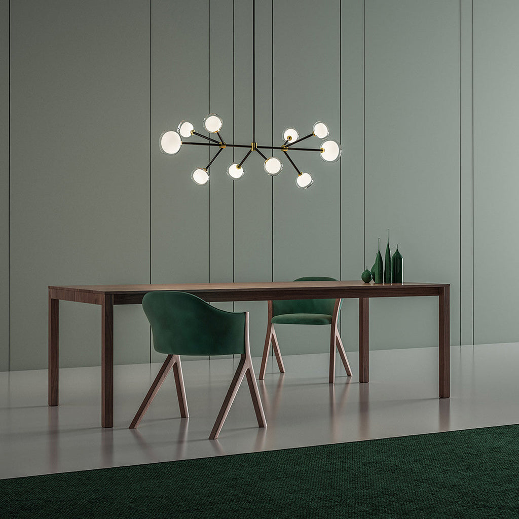Lit Clérachic chandelier with black arms and glowing glass globes, hung over a long walnut table with green chairs in a sage-green room.