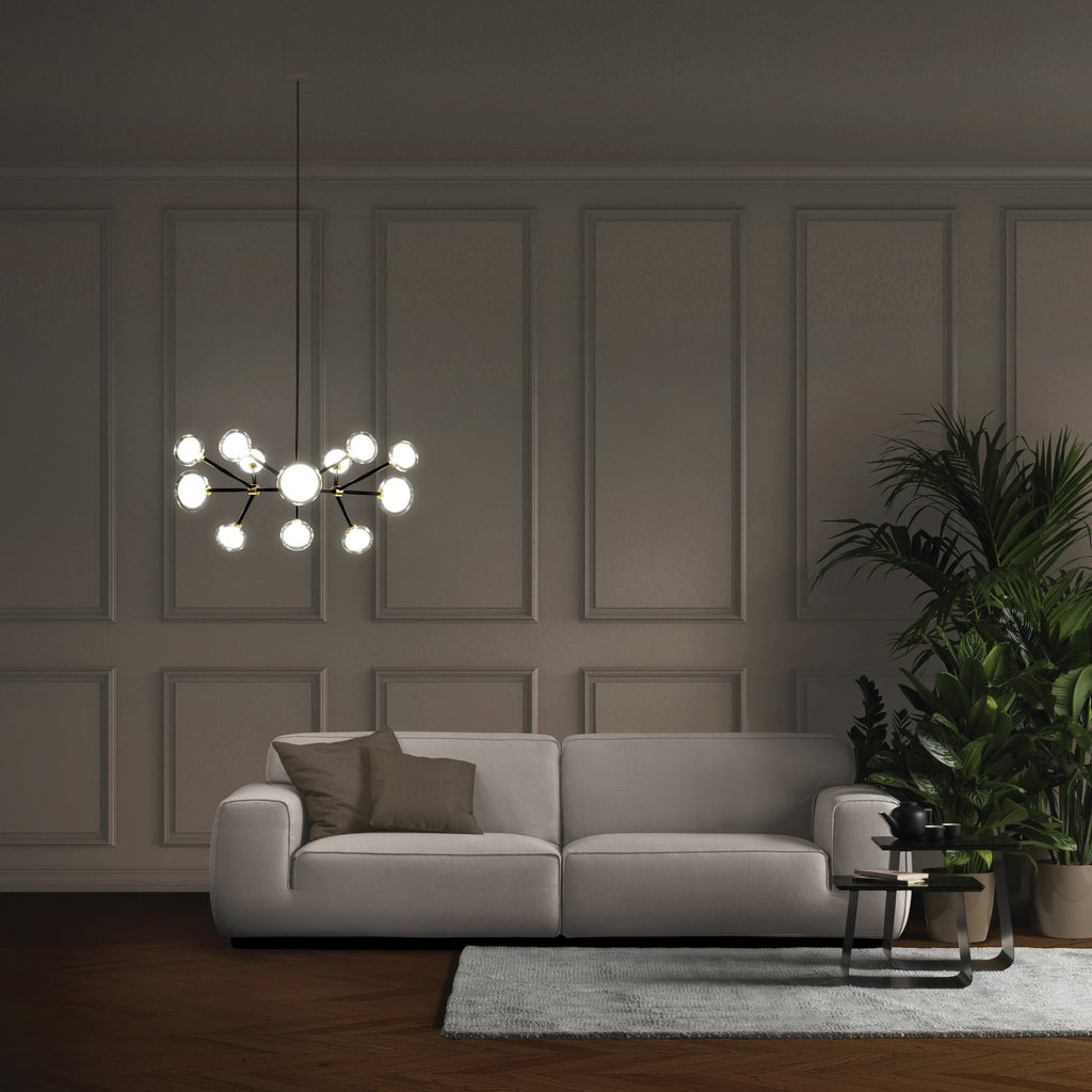 Lit Clérachic glass globe chandelier hanging in a dim panelled room above a pale grey sofa, with a leafy plant at the right.