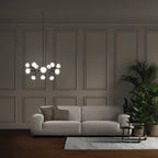Lit Clérachic glass globe chandelier hanging in a dim panelled room above a pale grey sofa, with a leafy plant at the right.