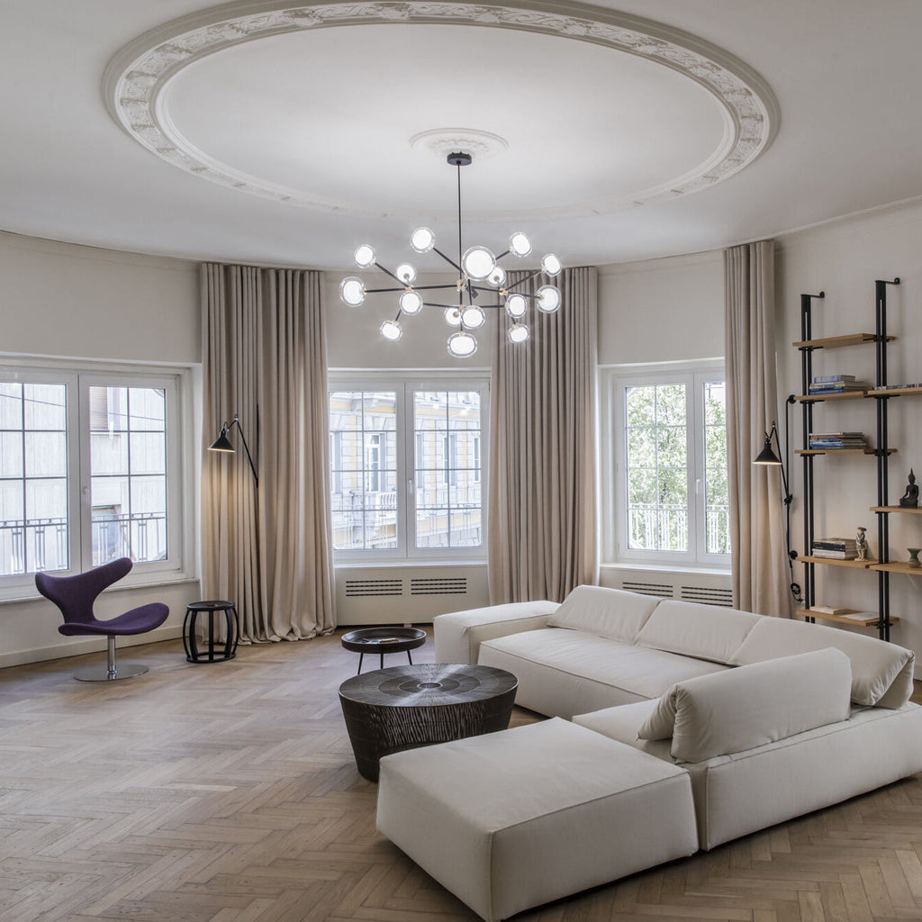 Clérachic glass globe chandelier below a decorative plaster ceiling rose in a living room with taupe curtains, a pale corner sofa and herringbone floor.