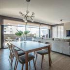 Clérachic chandelier with clear glass globes hanging in an open dining area, above a pale table with wooden chairs and a window onto a terrace.