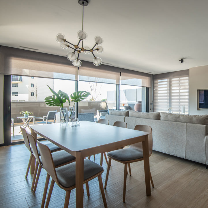 Clérachic chandelier with clear glass globes hanging in an open dining area, above a pale table with wooden chairs and a window onto a terrace.