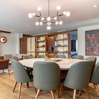 Lit Clérachic chandelier above a round marble dining table with grey-green leather chairs, in front of a walnut shelving wall.