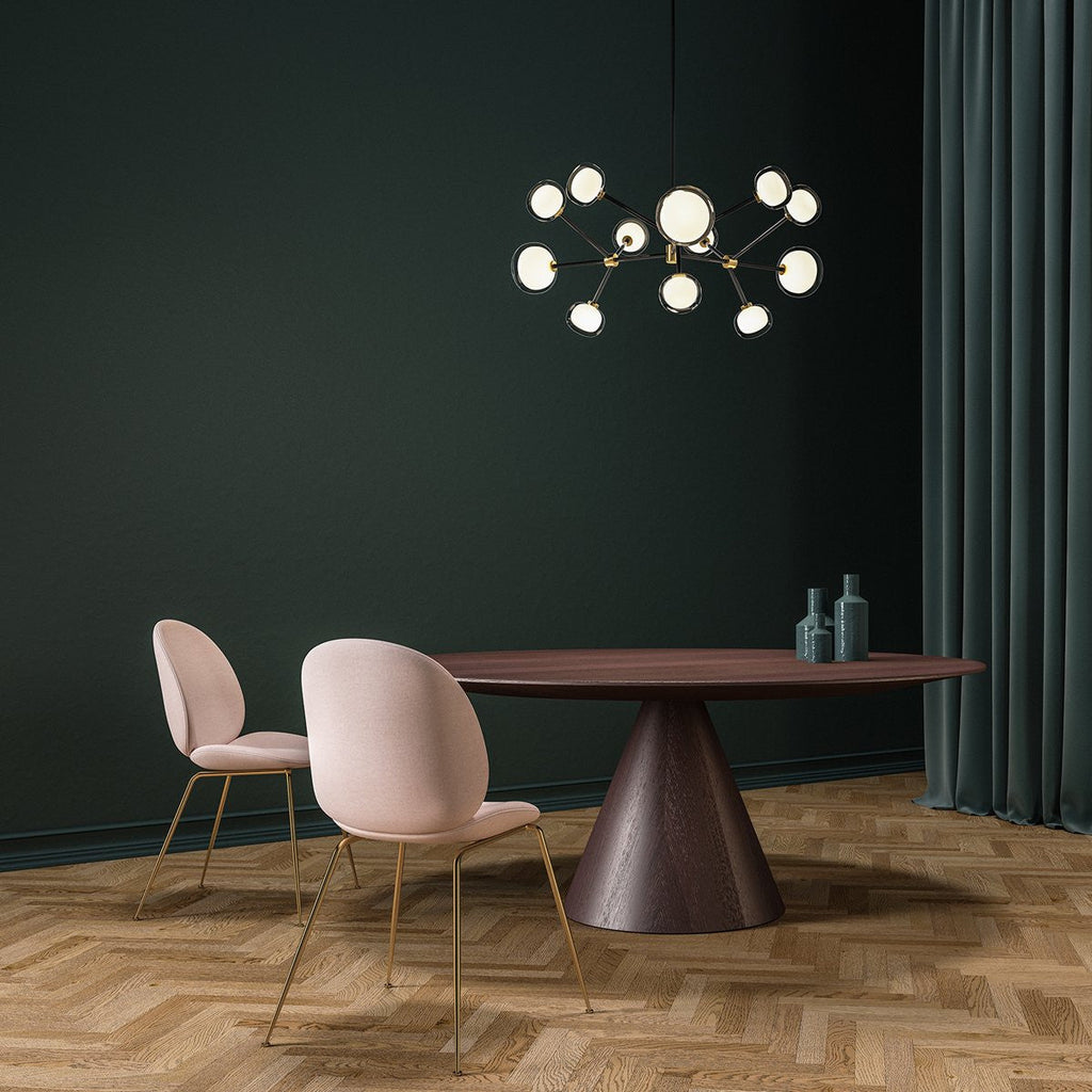 Clérachic chandelier lit against a deep green wall, over a round dark wood table with pink chairs on a herringbone floor.