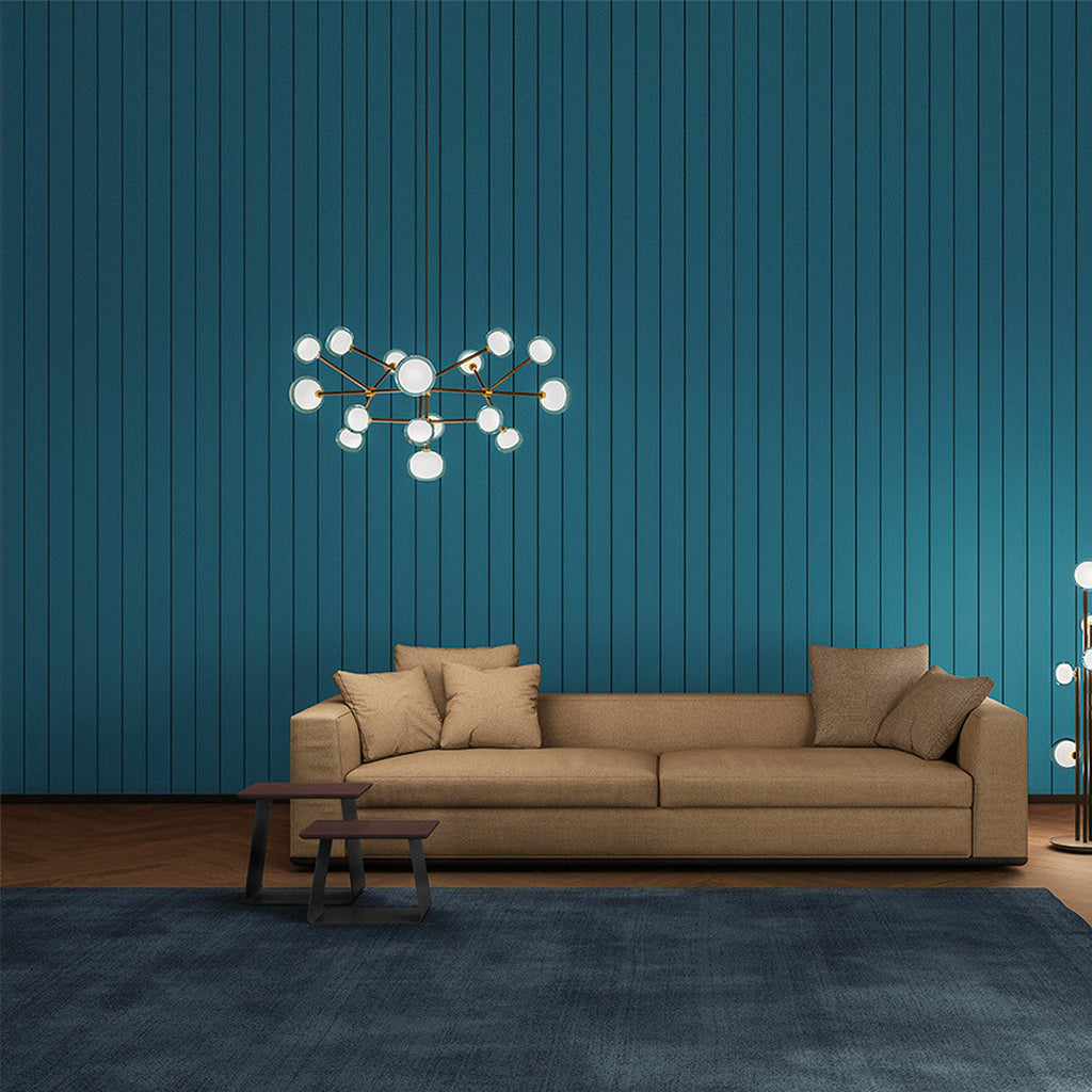Lit Clérachic chandelier on a teal slatted wall above a tan sofa, with a blue rug and two small tables.