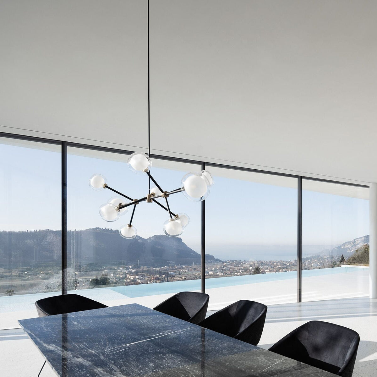 Clérachic chandelier with clear glass spheres on black arms, hung in front of floor-to-ceiling windows over a black marble dining table.