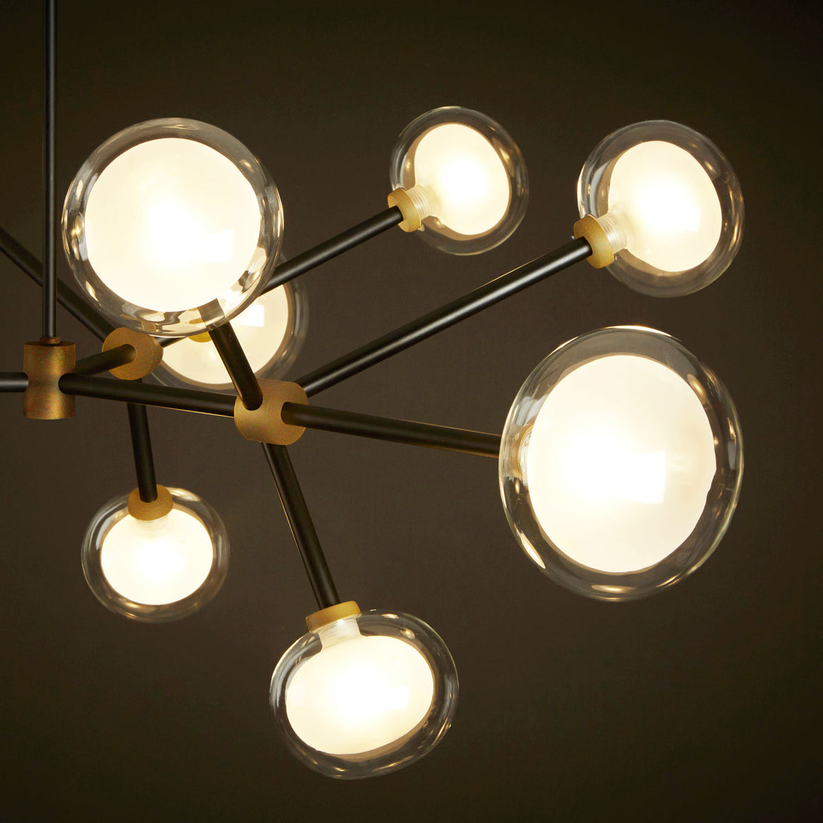 Close view of this Clérachic chandelier lit, with clear-rimmed glass globes glowing white on black arms with brass connectors.