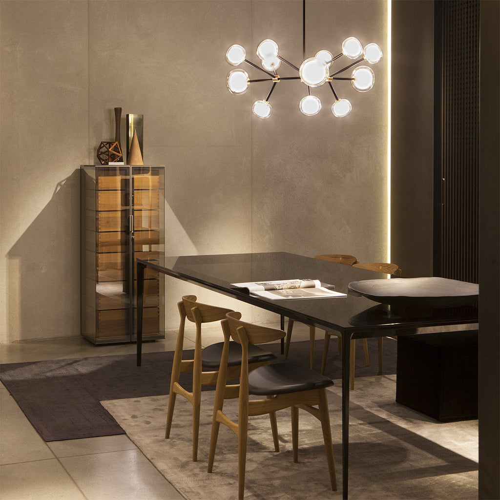 Clérachic chandelier lit with glass globes over a dark dining table and wooden chairs, beside a glass cabinet and a stone-toned wall.