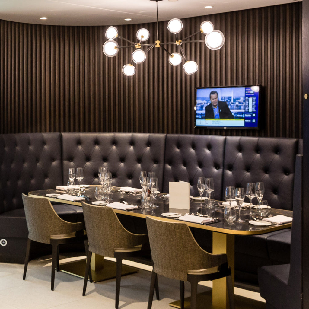 Lit Clérachic chandelier with glass globes in a restaurant booth, above a laid dark table with olive chairs and a tufted leather banquette.