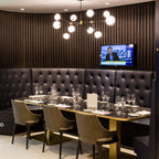 Lit Clérachic chandelier with glass globes in a restaurant booth, above a laid dark table with olive chairs and a tufted leather banquette.