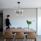 Clérachic chandelier with clear globes over a walnut dining table and chairs, with a blurred person walking past in a bright room.