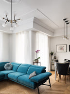 Clérachic chandelier with clear globes in the corner of a white room, near a teal velvet sofa and a dining area with black chairs.