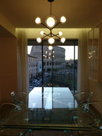 A Clérachic chandelier with a large central globe in a room with a glass dining table, and a view of an ancient amphitheatre through the window.
