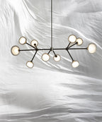 Clérachic chandelier with clear-rimmed glass globes on black arms, hung against rumpled white fabric from a thin black rod.