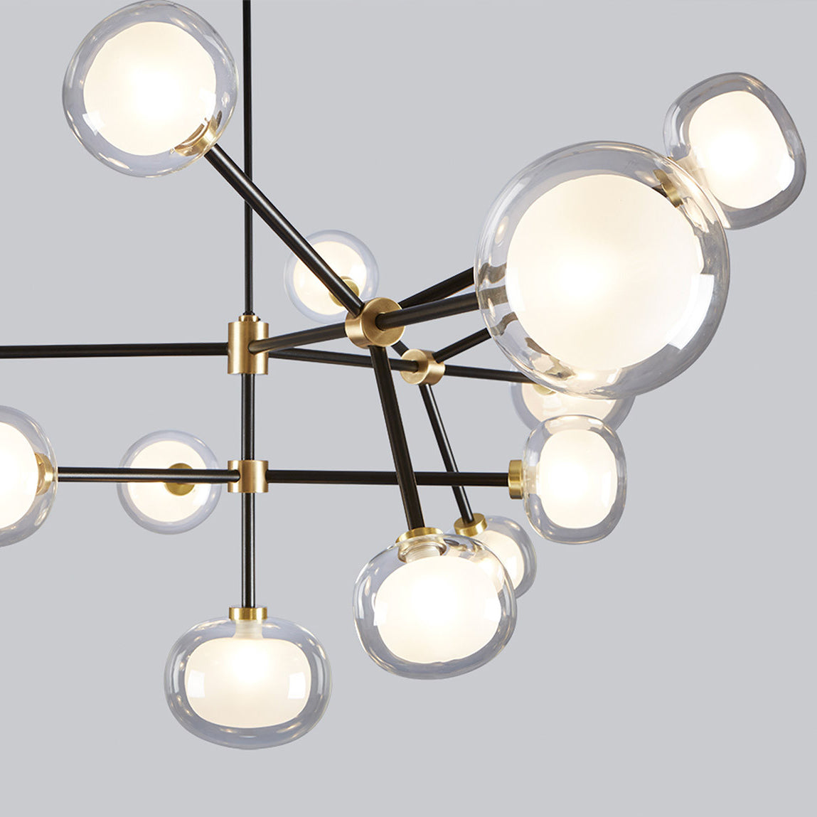Close view of the brass joints, black arms and clear glass globes with white inner shades of this Clérachic chandelier, on a grey backdrop.