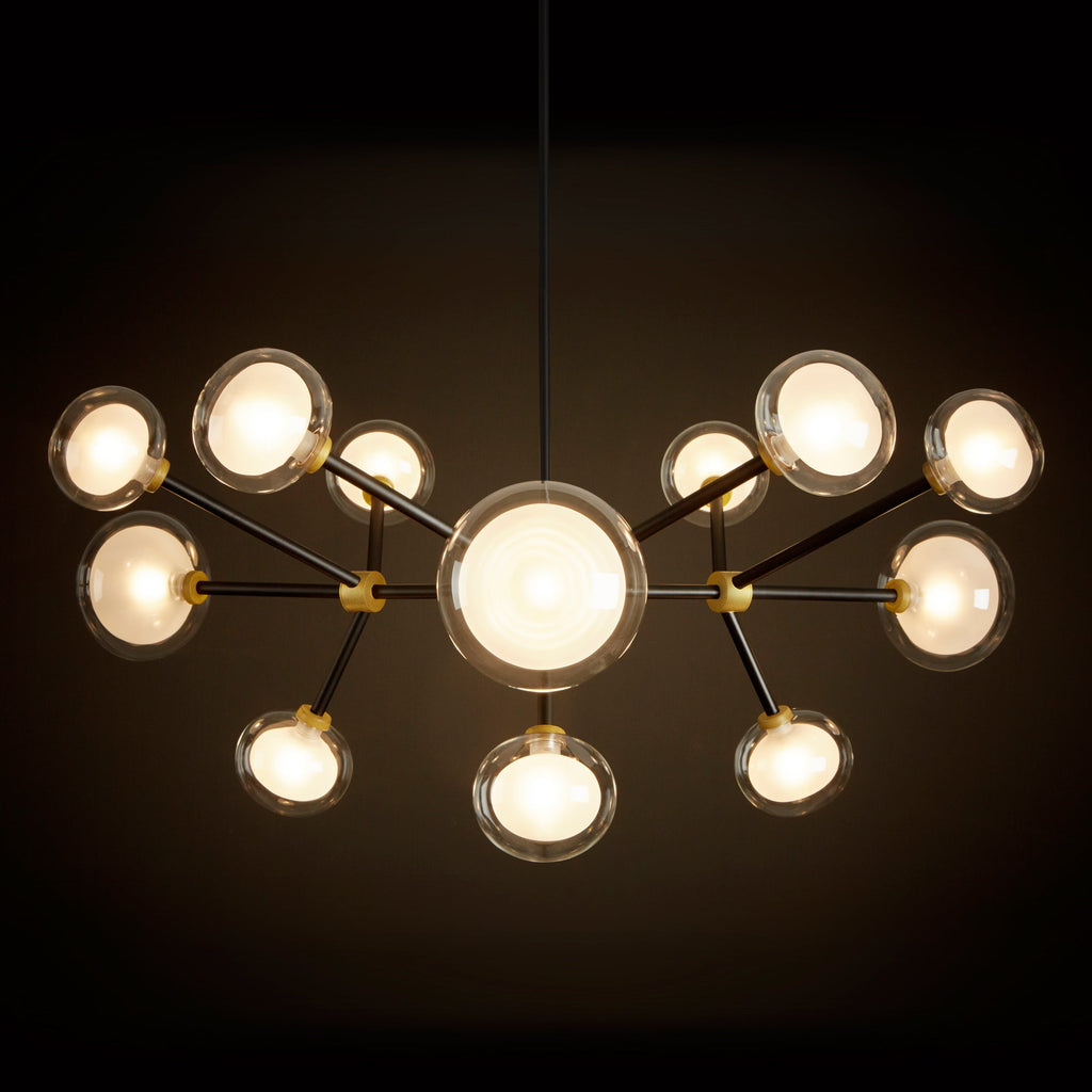 Clérachic chandelier glowing warm against a dark backdrop, with a large central globe and clear-rimmed shades on black arms.