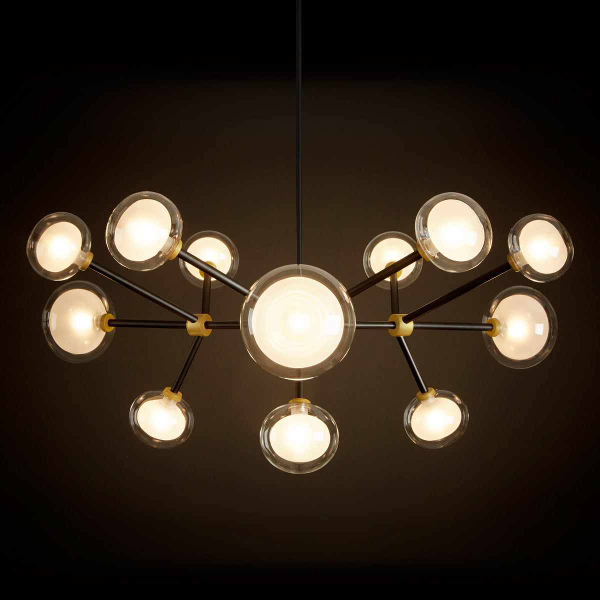 Clérachic chandelier glowing warm against a dark backdrop, with a large central globe and clear-rimmed shades on black arms.