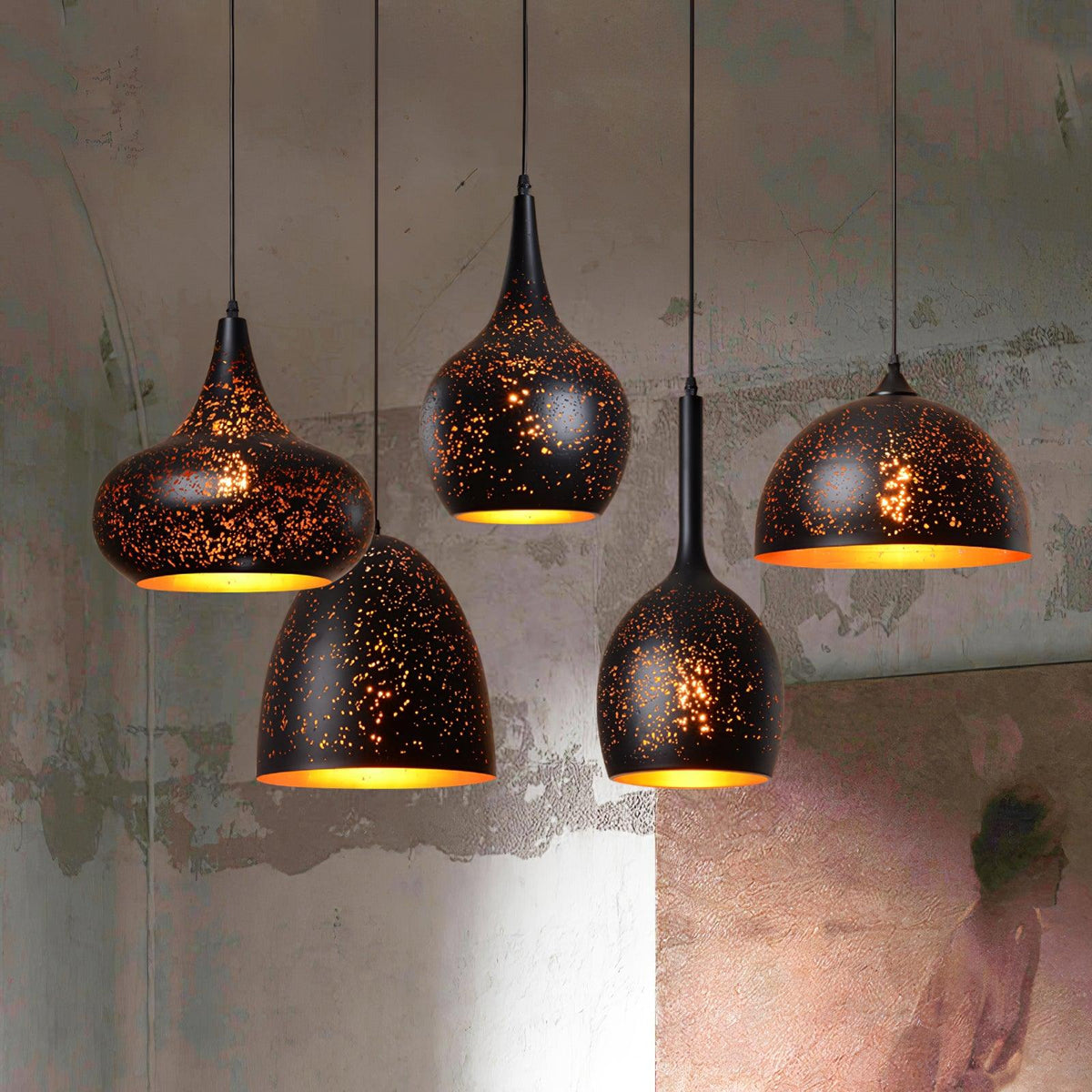 Cluster of four Clérachic black and gold pendants hanging at different drops against a rough grey plaster wall, their gold linings glowing.