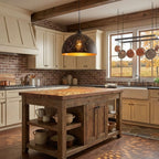 Domed Clérachic pendant with a perforated black shade hanging over a rustic timber kitchen island, with copper pans and a brick wall behind.