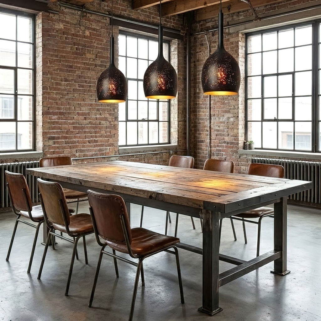Three narrow teardrop Clérachic pendants in a row above a long plank table with leather chairs, in a brick loft with tall steel windows.